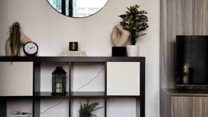 Un salon moderne avec un grand miroir rond, un téléviseur, une console ornée d’objets décoratifs et un tapis en cuir.