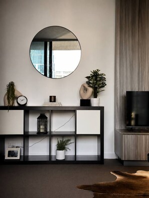 A modern living room with a round mirror, a TV, a console table with decorative items, and a leather rug. - Spacious 2BR City Views Retreat (Melbourne)