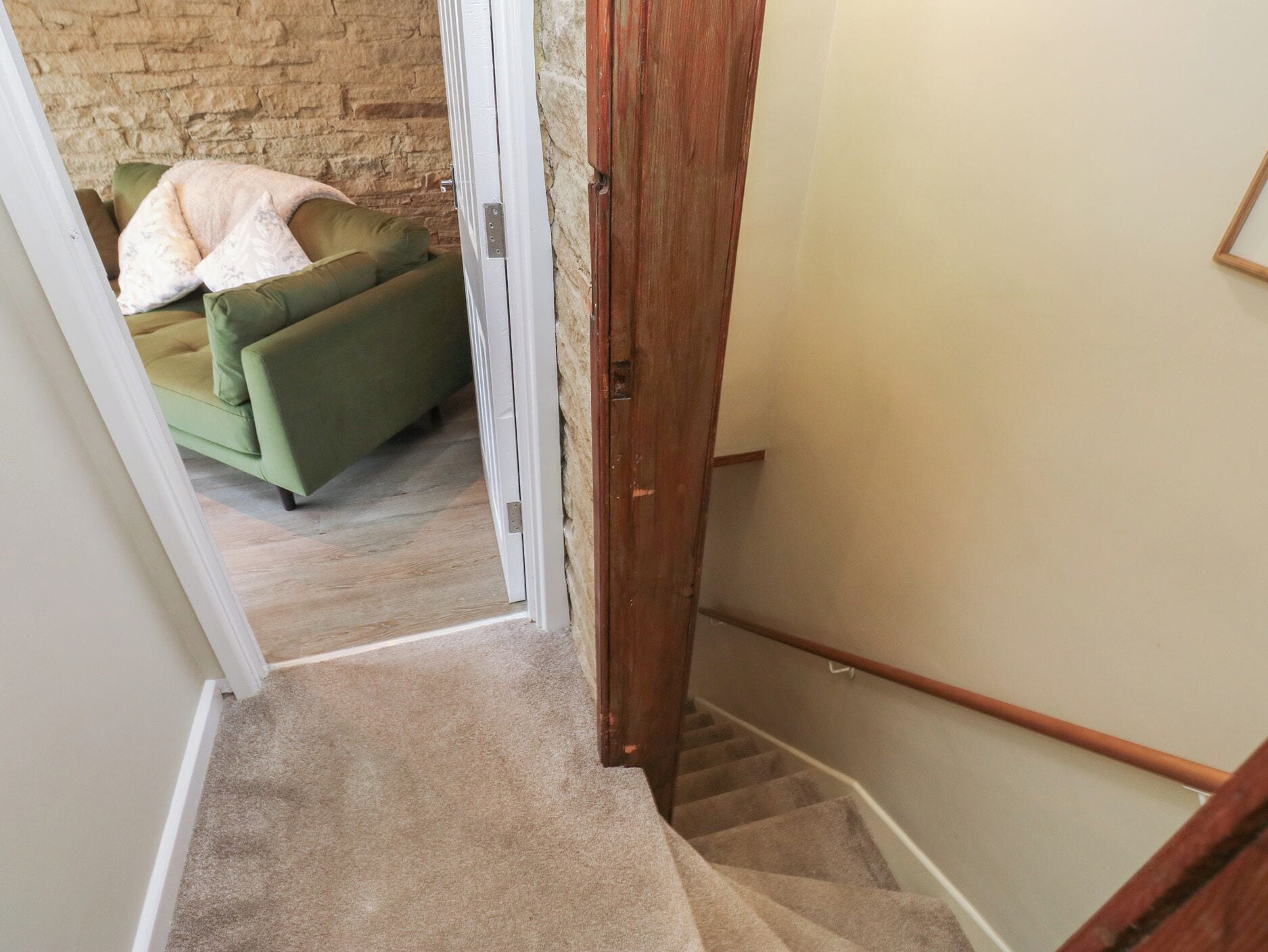 A carpeted staircase leading to a room with a green sofa and a brick wall.