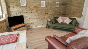Ein Wohnzimmer mit Steinsäule, einem grünen Sofa, einem braunen Ledersessel und einem Flachbildfernseher auf einem Holzboden.