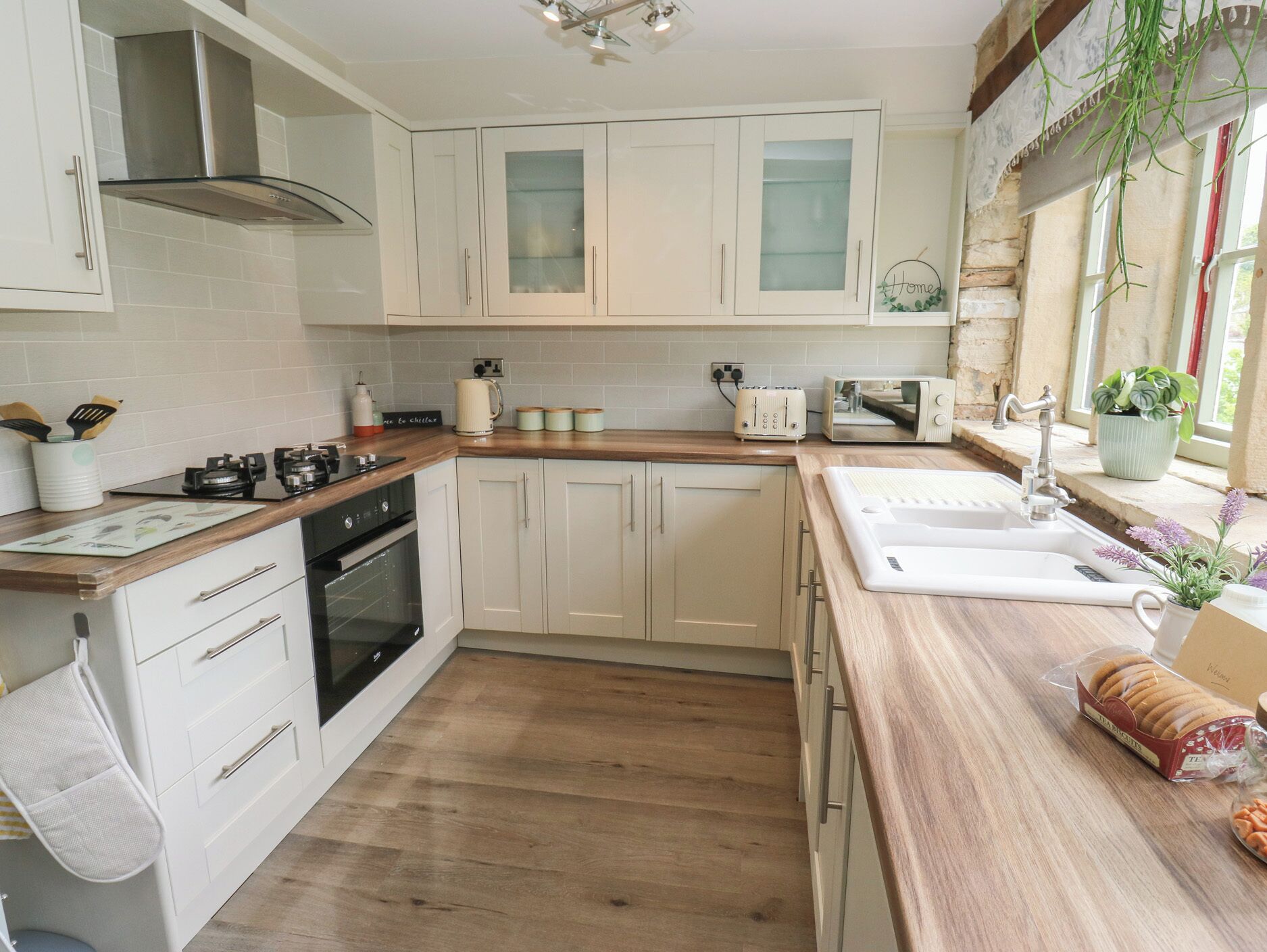 A kitchen with white cabinets, a wooden countertop, a stove, a sink, and a toaster.