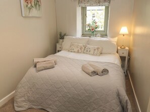 A neatly made bed with a quilted bedspread, two rolled towels, and floral-patterned pillows. - Riverview Cottage (Holmfirth)