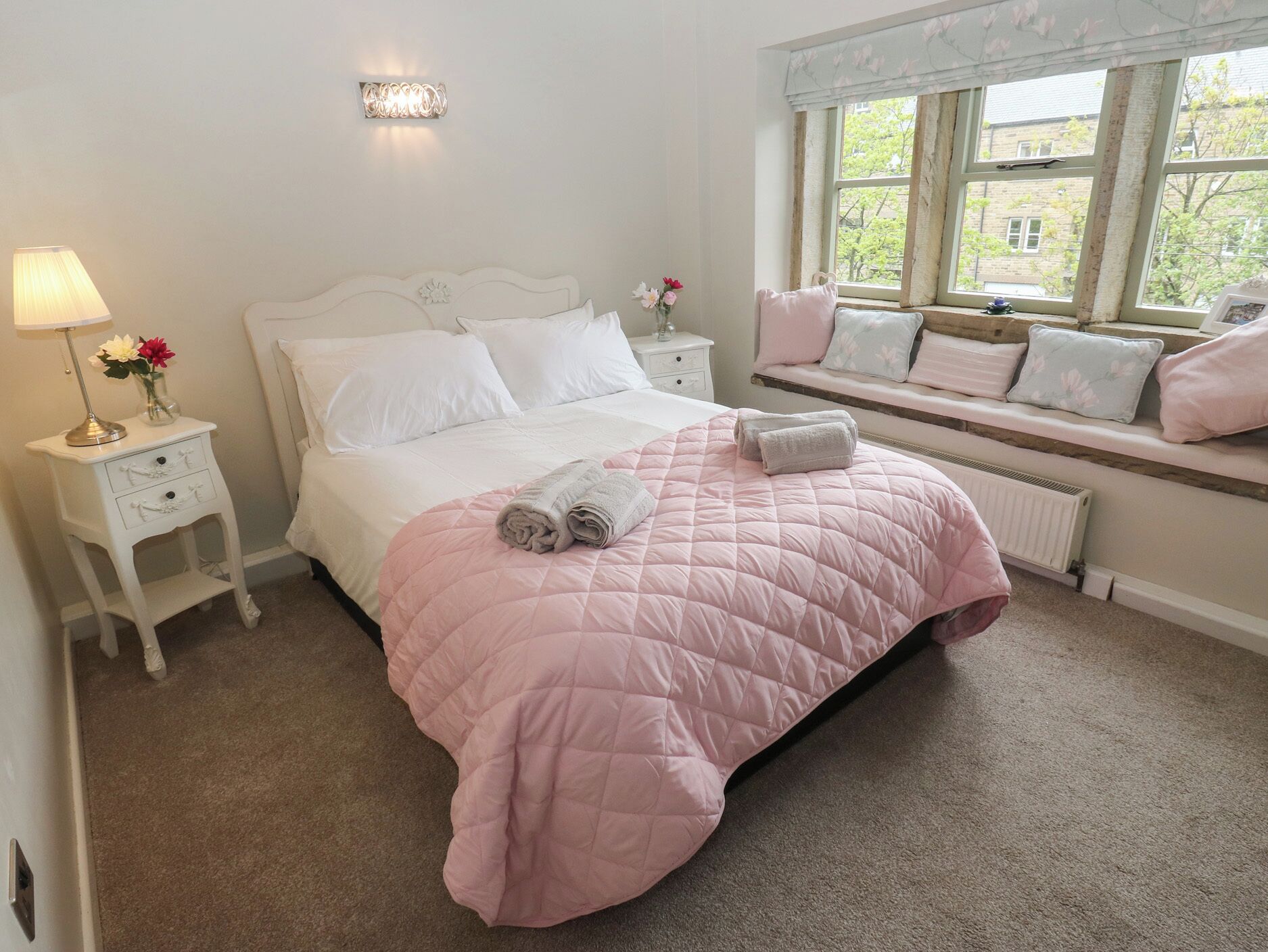 A bedroom with a bed, a bedside lamp, a nightstand, a window with a view, and a radiator.