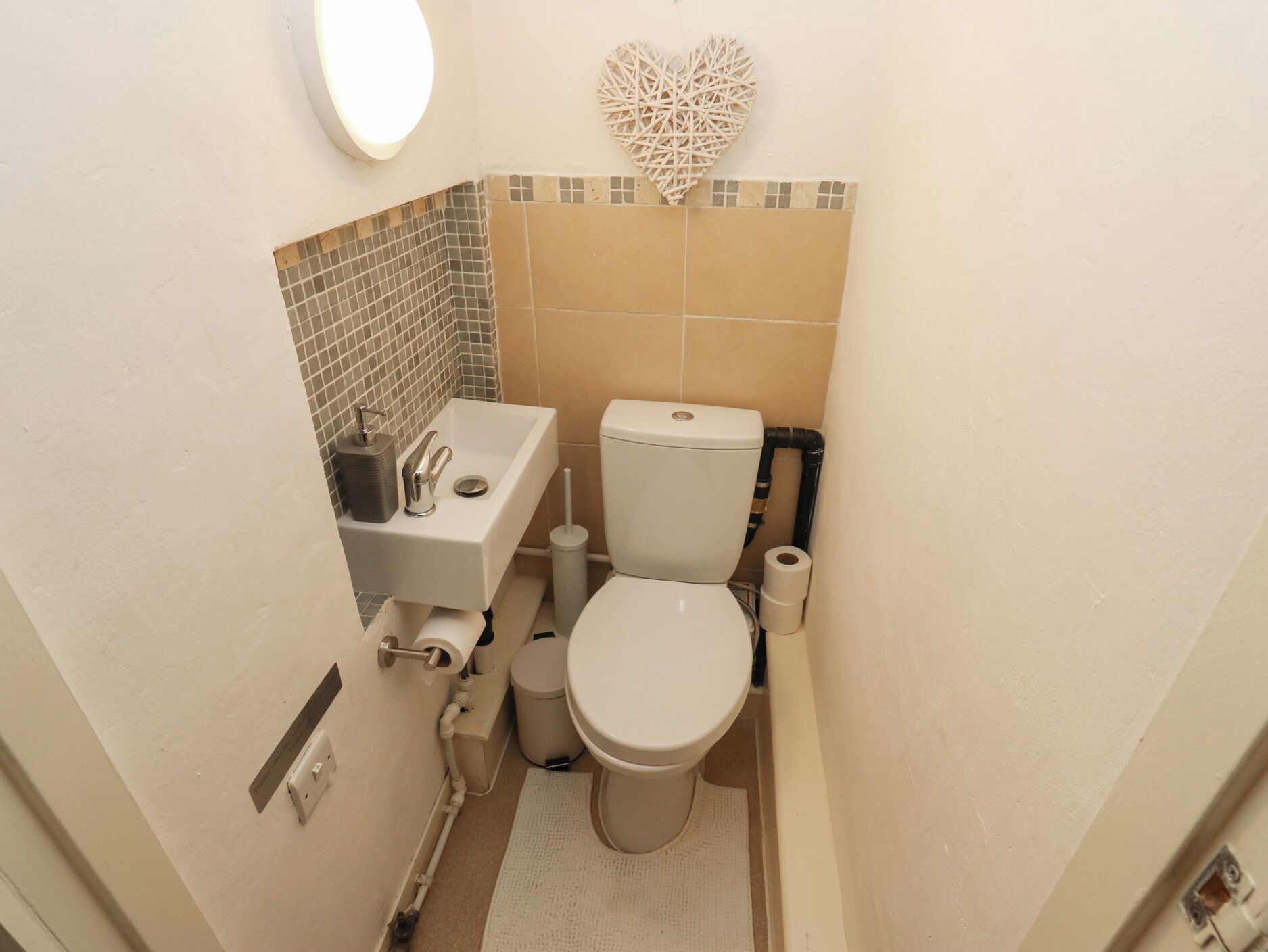 Ein kleines Badezimmer mit Waschbecken, Toilette und einer Wanddekoration in Herzform.
