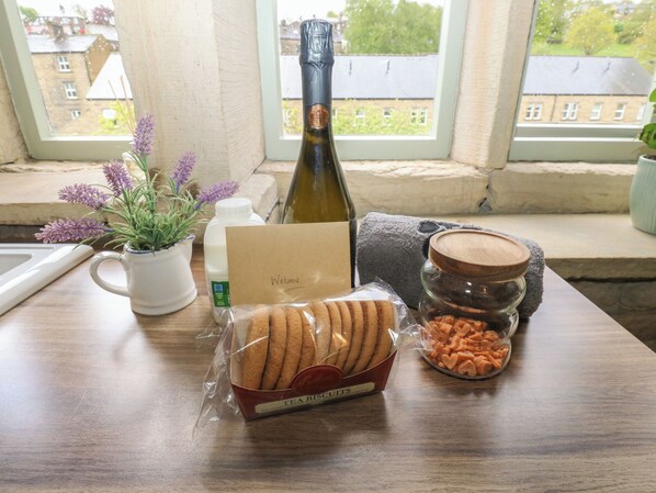 A table with a bottle, a card, a mug, a plant, and packaged snacks. - Riverview Cottage (Holmfirth)