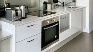 A modern kitchen with white cabinets, stainless steel appliances, and a glass backsplash. - Urban Skyline Escape (Melbourne)