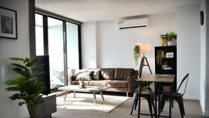 A modern living room with a sofa, coffee table, dining table, chairs, and potted plants. - Urban Skyline Escape (Melbourne)