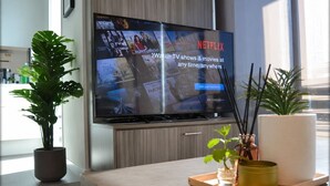 A modern living room with a flat-screen TV displaying a Netflix advertisement, a potted plant, a tray with a candle, and a large window. - Urban Skyline Escape (Melbourne)