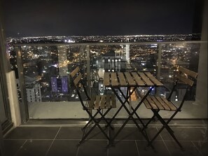 A balcony with a table and chairs, overlooking a cityscape at night. - 2BR Skyline Escape in Melbourne CBD (Melbourne)