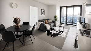 A modern living room with a dining area, a sofa, a coffee table, and a large window with a city view. - Central Melbourne Skyline Retreat (Melbourne)