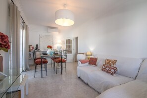 Un salon moderne comprenant un coin repas, un canapé agrémenté de coussins à motifs et un grand luminaire suspendu.
