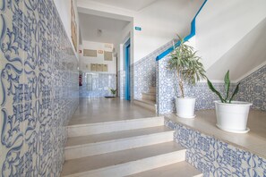 Corredor com azulejos estampados em azul, escadaria e plantas em vasos.