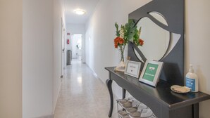 A reception desk with a welcome sign, a framed picture, a bottle of hand sanitizer, and a shoe rack. - Nora Quarteira Apartment T2 (Quarteira)