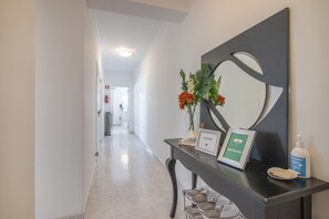 Uma receção com um letreiro de boas-vindas, um quadro emoldurado, um frasco de álcool em gel e um sapateiro.