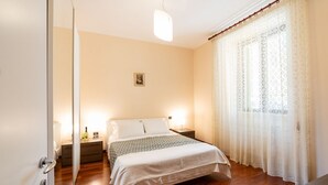 A bedroom with a bed, bedside tables, a nightstand, a lamp, and a window with curtains. - GuestHost - Comfy Apartment near the sea (Bisceglie)