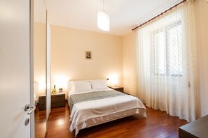 Ein Schlafzimmer mit Bett, Nachttischen, einer Lampe und einem Fenster mit Vorhängen.