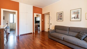 A living room with a sofa, wooden flooring, and a kitchen in the background. - GuestHost - Comfy Apartment near the sea (Bisceglie)