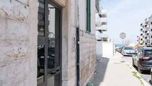 A building with a glass door, a visible window, and a street with parked cars. - GuestHost - Comfy Apartment near the sea (Bisceglie)