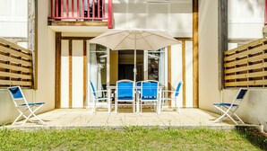 Une terrasse avec une table et des chaises, un balcon rouge et un parasol blanc.