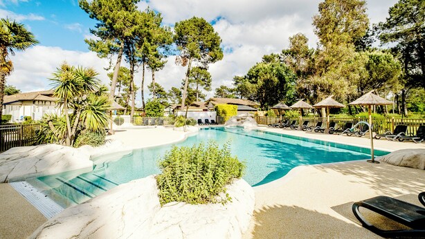 Une piscine entourée d’arbres, avec des chaises longues, sous un ciel dégagé.