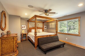 Un lit à baldaquin avec un ventilateur de plafond, une grande fenêtre avec des stores, une commode en bois et un banc.