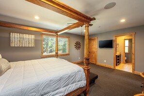 Ein Bett mit Himmelbett, ein Kopfteil, ein an der Wand befestigter Fernseher und ein Fenster mit Jalousien.