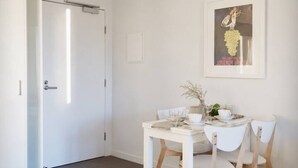 A minimalist dining area with a white table and chairs, a framed picture on the wall, and a door with a towel rack. - Prime Melbourne CBD View Apartment (Melbourne)