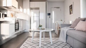 A modern kitchen with white cabinetry, a dining area with a white table, and a grey sofa. - Prime Melbourne CBD View Apartment (Melbourne)