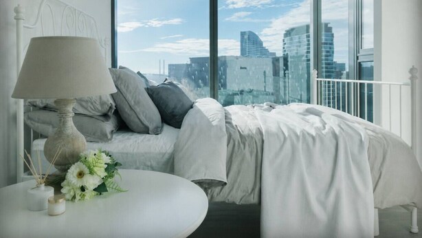 A bedroom with a city view, a bed with pillows, a lamp, and a small table with flowers. - Prime Melbourne CBD View Apartment (Melbourne)