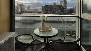 A balcony with a table and chairs, a vase with plants, and a cityscape view through large windows. - Prime Melbourne CBD View Apartment (Melbourne)