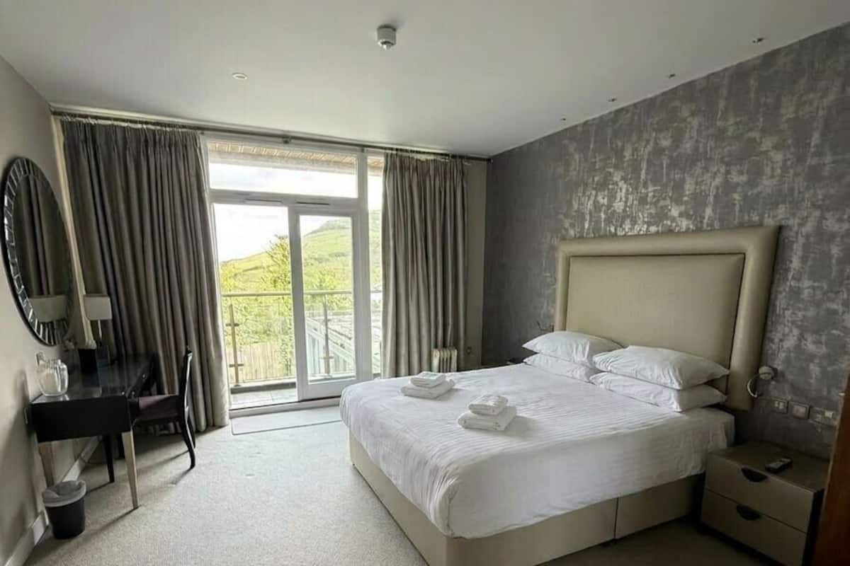 A hotel room with a large bed, a desk, a chair, a mirror, and a view of the outdoors.