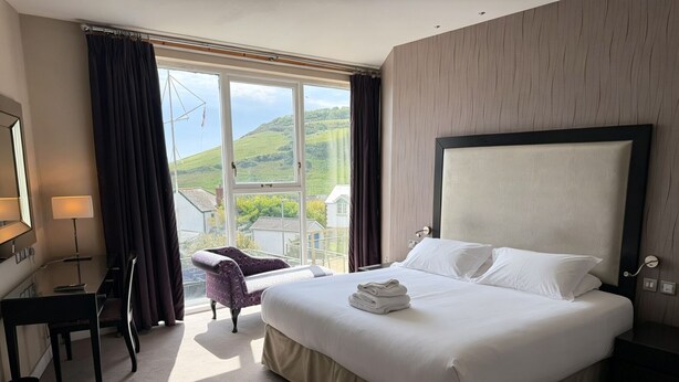 A hotel room with a large bed, a desk, a chair, and a view of the countryside. - Llawnroc Hotel (Gorran Haven)