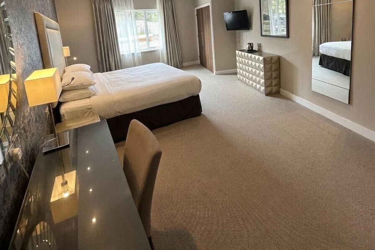 A hotel room with a bed, desk, chair, TV, and a large mirror.