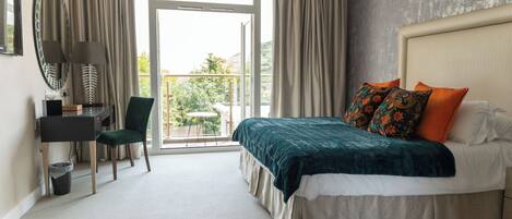 A hotel room with a bed, a desk, a chair, a small table, and a balcony with a view.