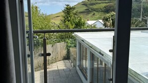 A balcony with a glass railing overlooking a hilly landscape and a clear sky. - Llawnroc Hotel (Gorran Haven)