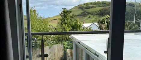 A balcony with a glass railing overlooking a hilly landscape and a clear sky.