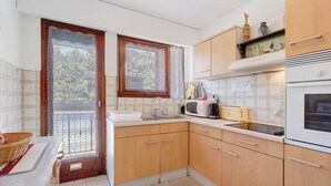 A kitchen with wooden cabinets, a microwave, a toaster, and a sink. - Roseraie Apartment with Private Pool, Wi-Fi, and Air Conditioning (Antibes)