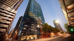 Een modern hoog gebouw met een glazen gevel, omringd door andere hoge gebouwen.