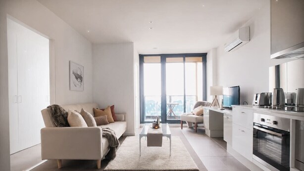 Een moderne woonkamer met een bank, een salontafel, en een eethoek met een tafel en stoelen. Er is een keuken met een fornuis en een koelkast.