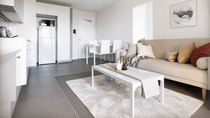 Een moderne, minimalistische woonkamer met een witte bank, een salontafel, en een eethoek met witte stoelen.