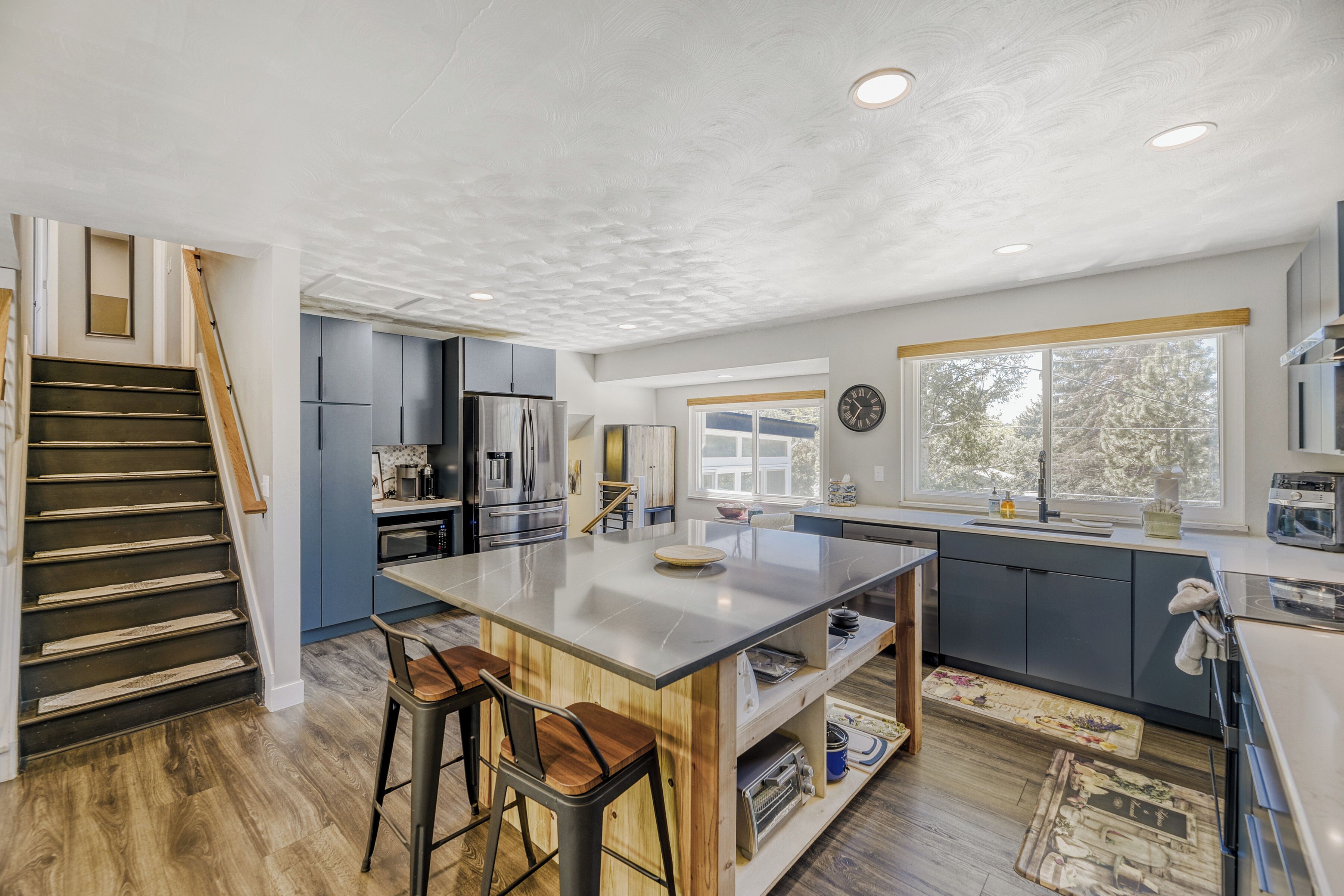 A modern kitchen with a central island, wooden bar stools, and a staircase.