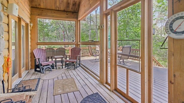 Een houten terras met Adirondack-stoelen, een tafel en een groot raam.