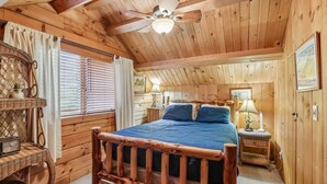 Een houten slaapkamer met een bed, nachtkastjes, een plafondventilator en een raam met blinds.