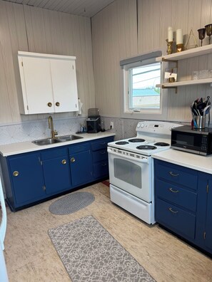 A kitchen with white cabinets, blue lower cabinets, a white stove, and a window.