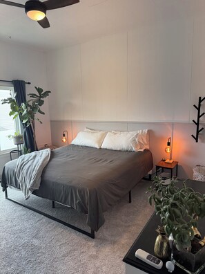 A modern bedroom with a bed, bedside lamps, a ceiling fan, and a potted plant.