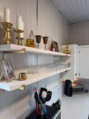 A kitchen with wooden shelves holding various items, a framed photo, and a microwave.