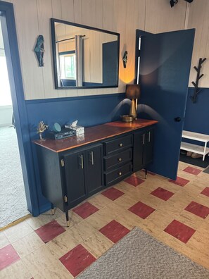 A room with a dark wooden cabinet, a mirror, a lamp, and a red and beige checkered floor.