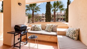 Ein Balkon mit Grill, Sitzgelegenheit und Blick auf Palmen und Gebäude.