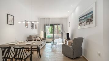 Een moderne woonkamer met een eethoek, een grijze fauteuil, een televisie en een schilderij aan de muur.