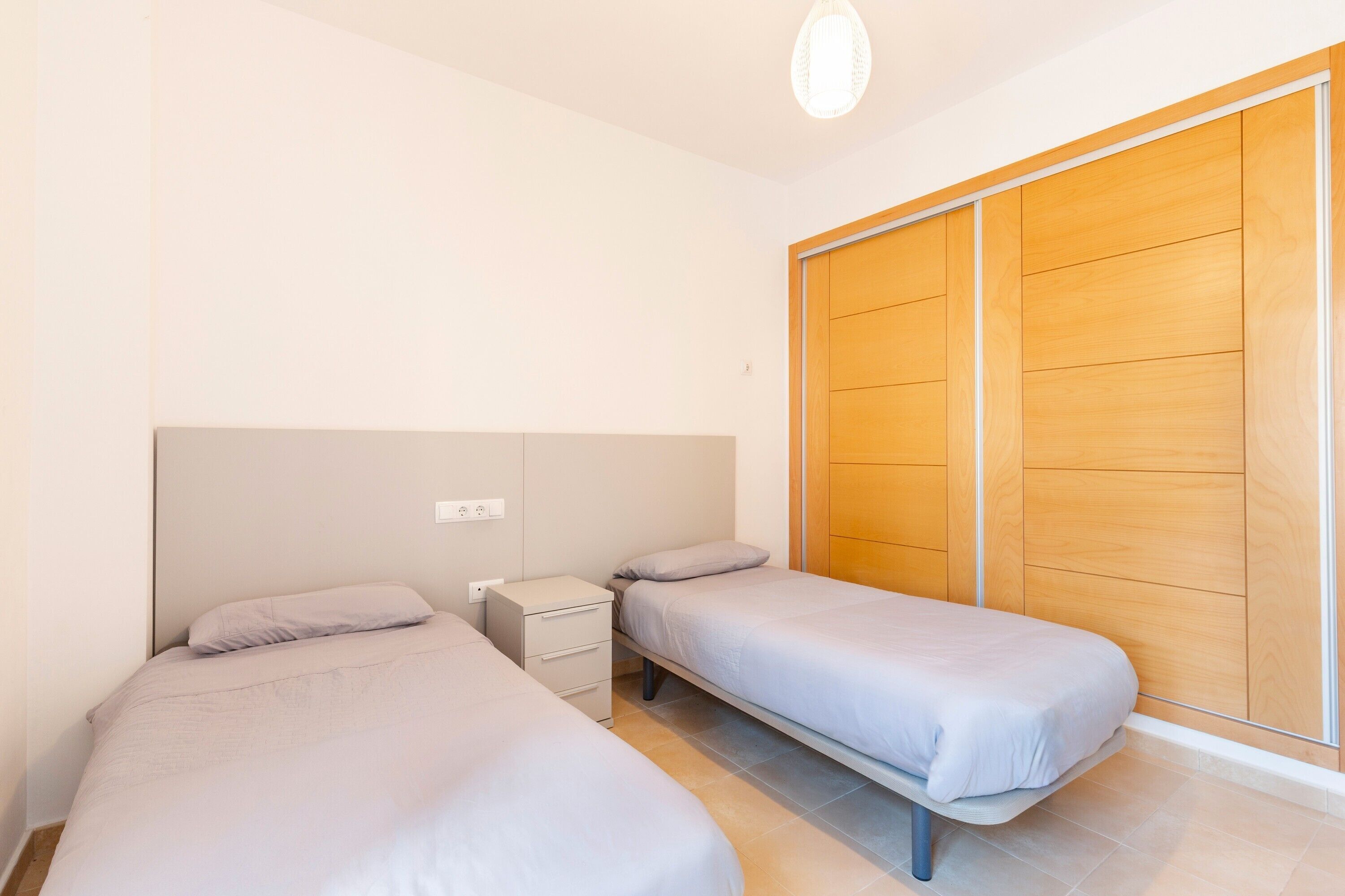 Een slaapkamer met twee eenpersoonsbedden, een nachtkastje, een houten garderobe en een lamp.